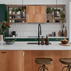 A modern kitchen island with wood grain cabinets and a white countertop, showcasing thoughtful kitchen styling with plants, fruit, and decorative items.