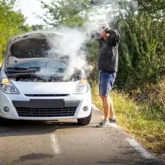 Mężczyzna z rozpaczą w rękach przy białym samochodzie, z którego bucha para. Rozbiegany diesel na poboczu drogi.