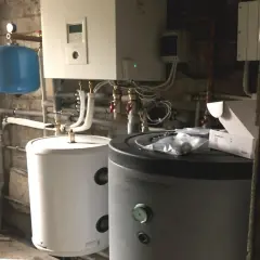 Podłączenie pompy ciepła do istniejącej instalacji. Widoczne zasobniki, sterownik i niebieski zbiornik wyrównawczy.
