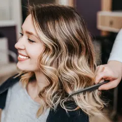 Sonrisa radiante con un balayage rubio natural, el cabello ondulado y con mechas doradas resalta su belleza.
