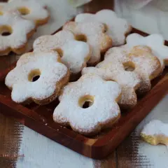 Deliziosi dolci solo tuorli benedetta, a forma di fiore, cosparsi di zucchero a velo su un vassoio di legno.