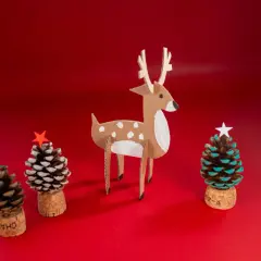 Julpynt med kottar: en papphjort och tre små julgranar gjorda av kottar, korkar och stjärnor.