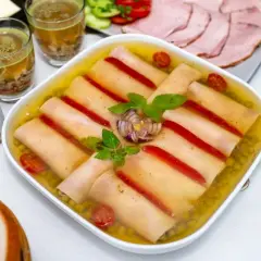 Szynka w galarecie z groszkiem i papryką, ozdobiona bazylią i cebulą. Obok plastry wędliny, pieczywo i sos.