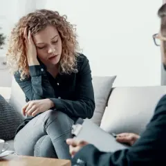 Kobieta z kręconymi włosami, przygnębiona, rozmawia z terapeutą. Dyskutują o tym, czym jest schizofrenia.