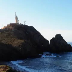 Faro en la cima de un acantilado rocoso sobre la cala del corralete. El mar azul choca contra las rocas.