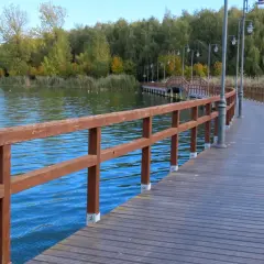 Drewniana kładka wije się nad wodą jeziora Chełmżyńskiego, otoczona jesienną zielenią.