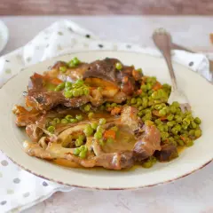 Un saporito ossobuco con piselli e carote, servito su un piatto bianco con tovagliolo a pois.