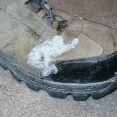 A dirty hiking boot with a white, foamy substance stuck to the side, possibly from a failed attempt to schuhsohle kleben (glue the shoe sole).