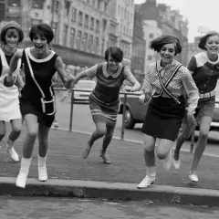 Cinco chicas con minivestidos y botas, al estilo de Mary Quant, corren alegres por la calle.