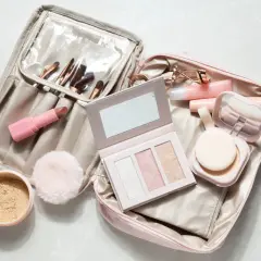 Une trousse de maquillage ouverte, prête pour un voyage en bagage cabine, révèle rouges à lèvres, pinceaux, palette et poudrier.