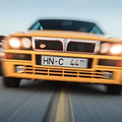 Żółta Lancia Delta Integrale pędzi na drodze, wyprzedzając inne samochody.