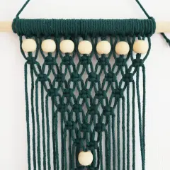 Tenture murale en macramé vert foncé avec perles en bois sur une tige en bois.