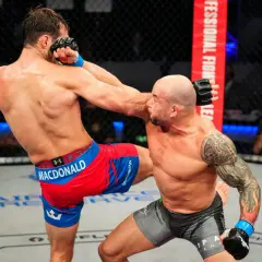 En MMA-fighter med tatueringar på armen, likt Gleison Tibau, tar emot en spark i ansiktet.