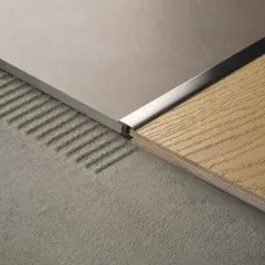 Dettaglio di profili piastrelle dopo posa, con finitura metallica che separa un pavimento in gres grigio da uno in legno.