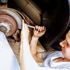 Meccanico lavora su un disco freno arrugginito, forse per diagnosticare i sintomi di un cuscinetto ruota rotto.