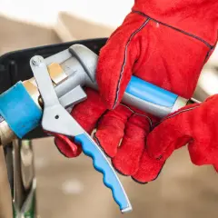 Ręce w czerwonych rękawicach podłączają pistolet do tankowania LPG. Sprawdzanie aktualnej lpg cena to klucz do oszczędności.