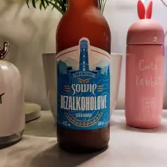 Butelka piwa Sowie Bezalkoholowe 0,5% obok różowego termosu z uszami królika i lampki w kształcie jelonka.