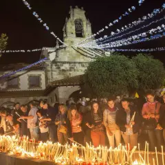 Multitud enciendiendo velas frente a una iglesia iluminada por guirnaldas, parte de las fiestas de Revilla de Camargo.