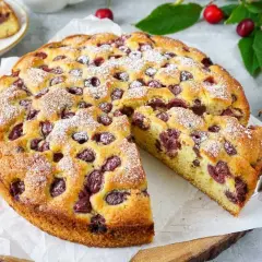 Saftiger kirschkuchen mit frischen kirschen, bestäubt mit Puderzucker. Ein Stück wurde bereits herausgeschnitten.