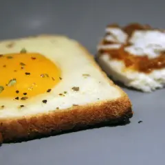 Une tranche de pain de mie avec un œuf au plat et des herbes. Une autre tranche est à côté, tartinée. Recette pain de mie œuf poêle facile.