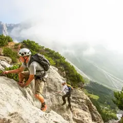 Dwóch turystów pokonuje via ferrata w Austrii, wspinając się po skalnej ścianie z ubezpieczeniem stalowej liny.