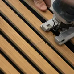 Mani che guidano un seghetto alternativo per tagliare pannelli fonoassorbenti in legno.