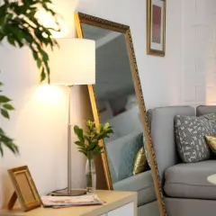 Ein großer Spiegel und eine Stehlampe machen die dunkle Wohnung heller. Ein Sofa mit Kissen und ein kleiner Tisch mit Kerze sind zu sehen.