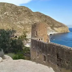 Ruinas de un castillo en cala san pedro, con el mar azul y montañas al fondo.