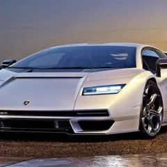 Biały Lamborghini Countach L, ikona motoryzacji, prezentuje swoje ostre linie na tle zachodzącego słońca.