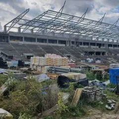 Budowa stadionu RKS Radomiak Radom w toku. Betonowe trybuny i stalowa konstrukcja dachu, wokół materiały budowlane.