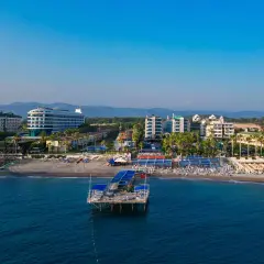 Widok na plażę Concordia Celes Beach z molo, hotelami i palmami w tle.