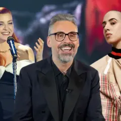 Tre cantanti calabresi sorridono: una con capelli rossi e abito bianco e nero, un uomo con occhiali e giacca scura, e una giovane con testa rasata e giacca beige.