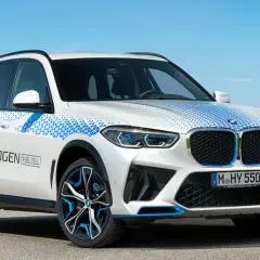 Białe BMW X5 z niebieskimi akcentami i napisem "BMW HYDROGEN FUEL CELL" na drzwiach, symbolizujące przyszłość motoryzacji.