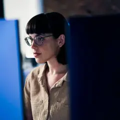 Junge Frau mit Brille und Kurzhaarschnitt, konzentriert auf einen Bildschirm. Sie repräsentiert eine der vielen Berufe mit Zukunft in der digitalen Welt.