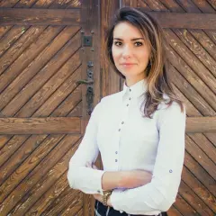 Kobieta w białej koszuli stoi przed drewnianymi drzwiami.