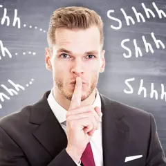 Uomo d'affari con dito sulle labbra, circondato da "Shhh..." scritti sulla lavagna. Il silenzio assenso significato è chiaro: non parlare.