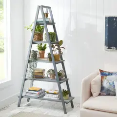Perchero escalera gris con plantas y libros, junto a un sofá rosa.