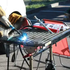 Spawanie aluminium migomatem. Jasny łuk spawalniczy rozświetla metalowe elementy na stole warsztatowym.