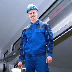 Ein Handwerker in blauer Arbeitskleidung und Helm trägt einen Werkzeugkasten. Er ist bereit für den Einsatz nach DIN 14677.