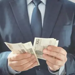 Mężczyzna w garniturze liczy banknoty 100 zł. Czy to jego zarobki jako członka rady osiedla?