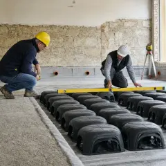 Operai installano elementi per vespaio pavimento, usando livella per garantire la planarità.
