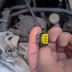 Wtyczka z żółtym wkładem, być może związana z błędem **dtc p1693 volkswagen**. W tle widać fragmenty silnika.