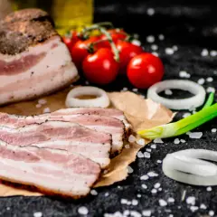 Idealny boczek do carbonary: plastry wędzonego boczku, pomidorki, cebula i szczypiorek na czarnym tle.