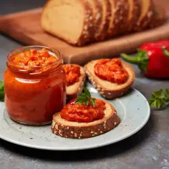 Słoik pełen pysznego sosu paprykowego, podany z chlebem i świeżymi paprykami. Idealny na przekąskę!