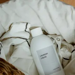 Una botella de líquido para la colada descansa entre la ropa blanca, lista para que el lino se dé de sí.