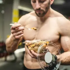 Un homme musclé mange un repas sain dans une salle de sport. Il utilise des protéines végétales pour sa musculation.