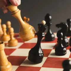 Ręka przesuwa jasnego króla, by zbić czarnego króla. Strategia jak sprzedać akcje.
