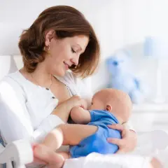 Uśmiechnięta mama karmi piersią dziecko w bujanym fotelu. Dobra dieta przy karmieniu piersią to podstawa.