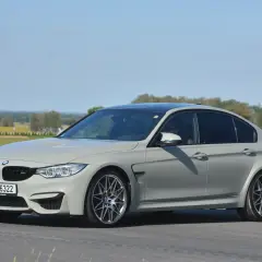 Szare BMW M3 F80 na torze wyścigowym, z widocznym kierowcą.