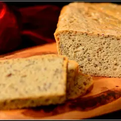 Chleb z siemienia lnianego, pokrojony na kromki, leży na drewnianej desce. Obok niego czerwona, zwiewna tkanina.